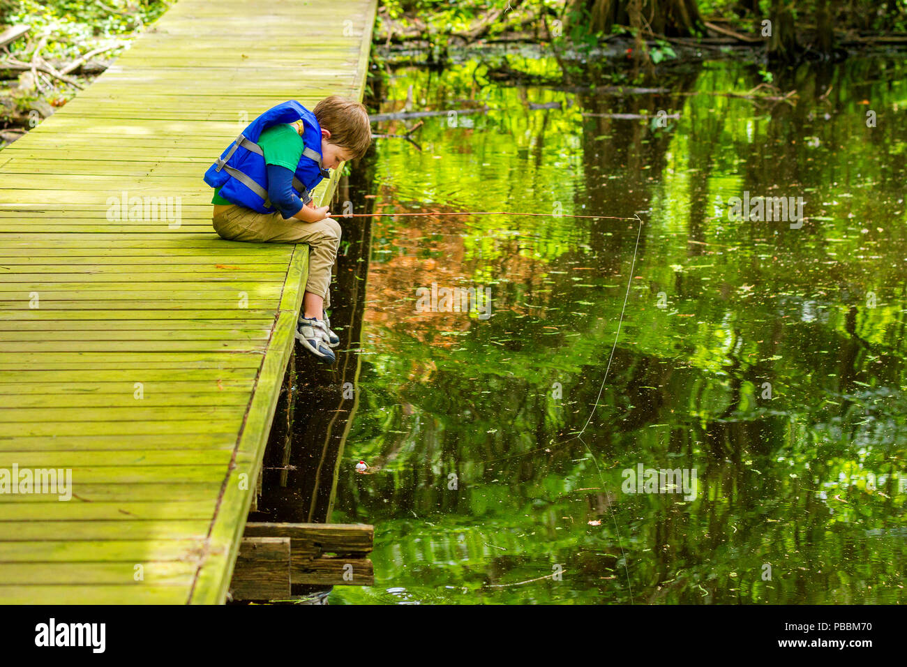 Eine ungeduldige Junge, Angeln Junge starrt auf seine noch Bobber, bereit, ihn zu bewegen, da er beugt sich über den Rand des Dock er fischen aus am See Bisti Stockfoto