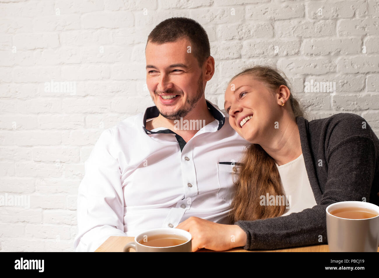 Das Mädchen und der Kerl in Cafe, an einem Tisch, reden. Das Mädchen den Kopf auf der Schulter zum Kerl, sie lachen. Stockfoto