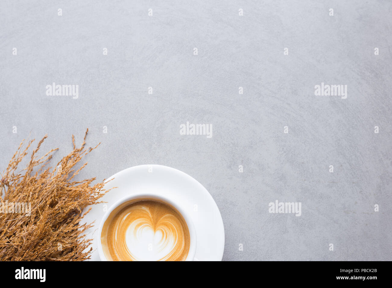 Eine Tasse Kaffee Latte auf weiße Tasse mit getrockneten Blumen auf Betonboden und Platz für Ihren Text Stockfoto