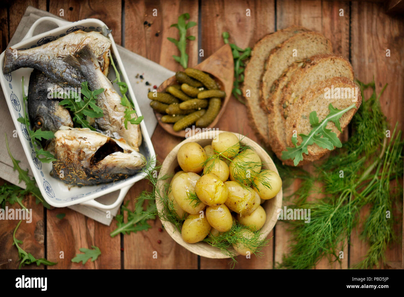 Mittagessen. gebackene Dorado und jungen Kartoffeln. Marinierten Gurken und Schwarzbrot. Im rustikalen Stil, Stockfoto