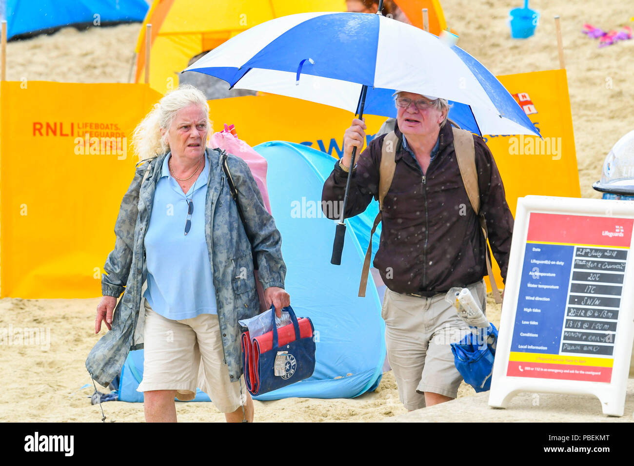 Lyme Regis, Dorset, Großbritannien. 28. Juni 2018. UK Wetter. Urlauber Unterschlupf unter einem Regenschirm verlassen den Strand als der Regen beginnt in den Badeort Lyme Regis am ersten Tag der Hauptversammlung der Stadt RNLI lifeboat Woche an einem kühlen, windigen Tag. Foto: Graham Jagd-/Alamy leben Nachrichten Stockfoto