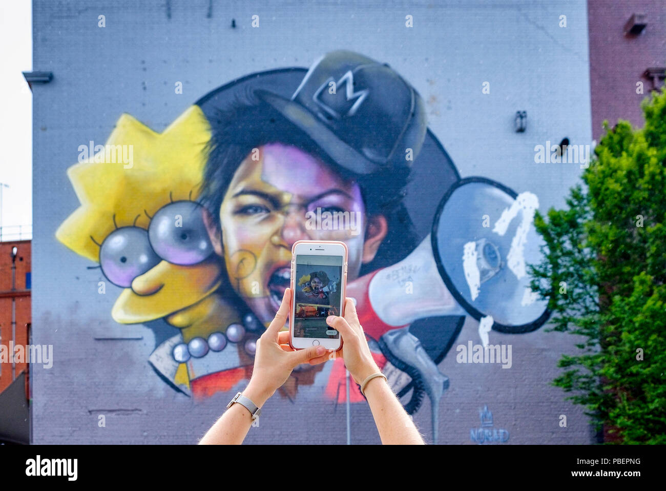 Bristol, Großbritannien. Juli 2018. Eine Frau wird abgebildet, als sie mit ihrem Mobiltelefon ein Foto von Nomad Clans riesengroßem lisa simpson Kunstwerk auf der Seite der Tabakfabrik in Bedminster macht. Das Upfest, das an drei Tagen stattfindet, ist Europas größtes Free Street Art & Graffiti Festival und ist nun in seinem zehnten Jahr. Kredit: Lynchpics/Alamy Live News Stockfoto
