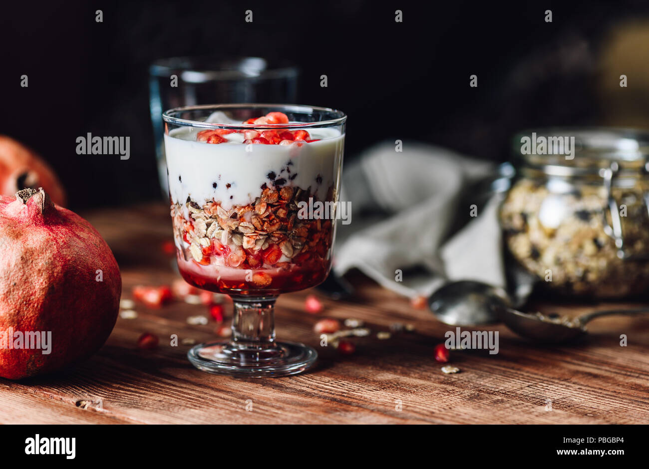 Granatapfel-Parfait mit einigen Zutaten auf Hintergrund. Serie über bereiten gesundes Dessert mit Granatapfel, Müsli, Cream und Jam. Stockfoto