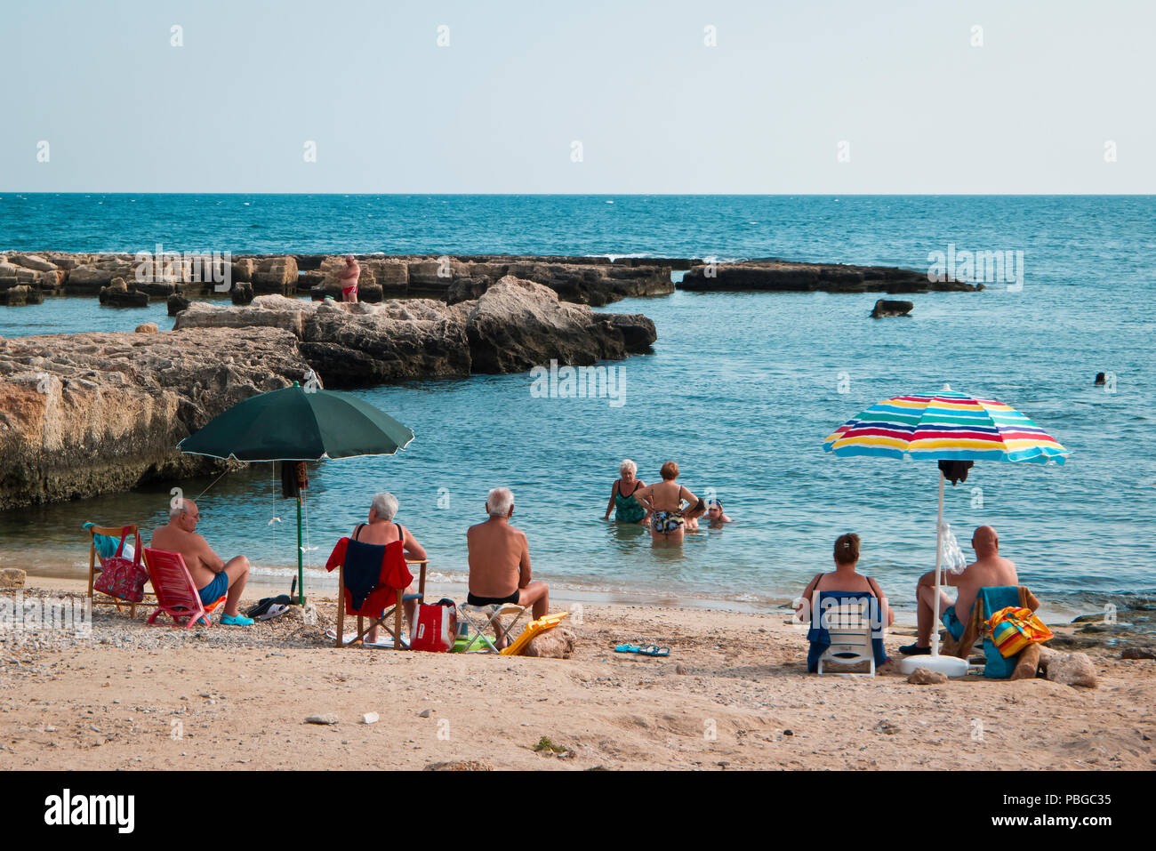 Monopoli, Italien, 07/26/2018; Gruppe von Senioren an einem warmen Sommermorgen, am Strand von Monopoli, dass Sie die kühle Entspannung genießen werden. Stockfoto