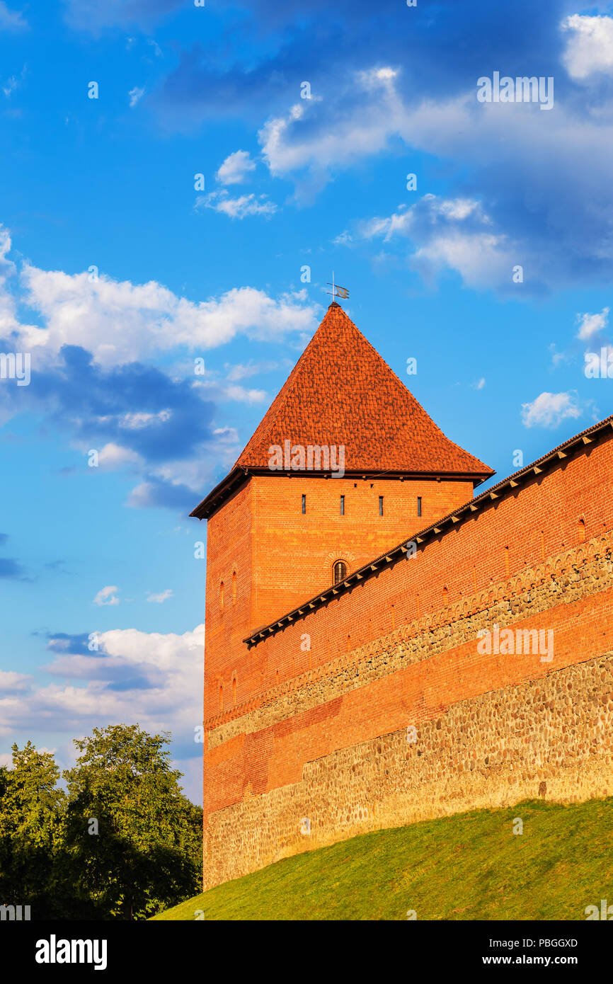Ein mächtiger Turm der Lida Burg aus rotem Backstein und Stein leuchtet mit der Sonne gegen einen schönen aber stürmischen Himmel, Weißrussland Stockfoto