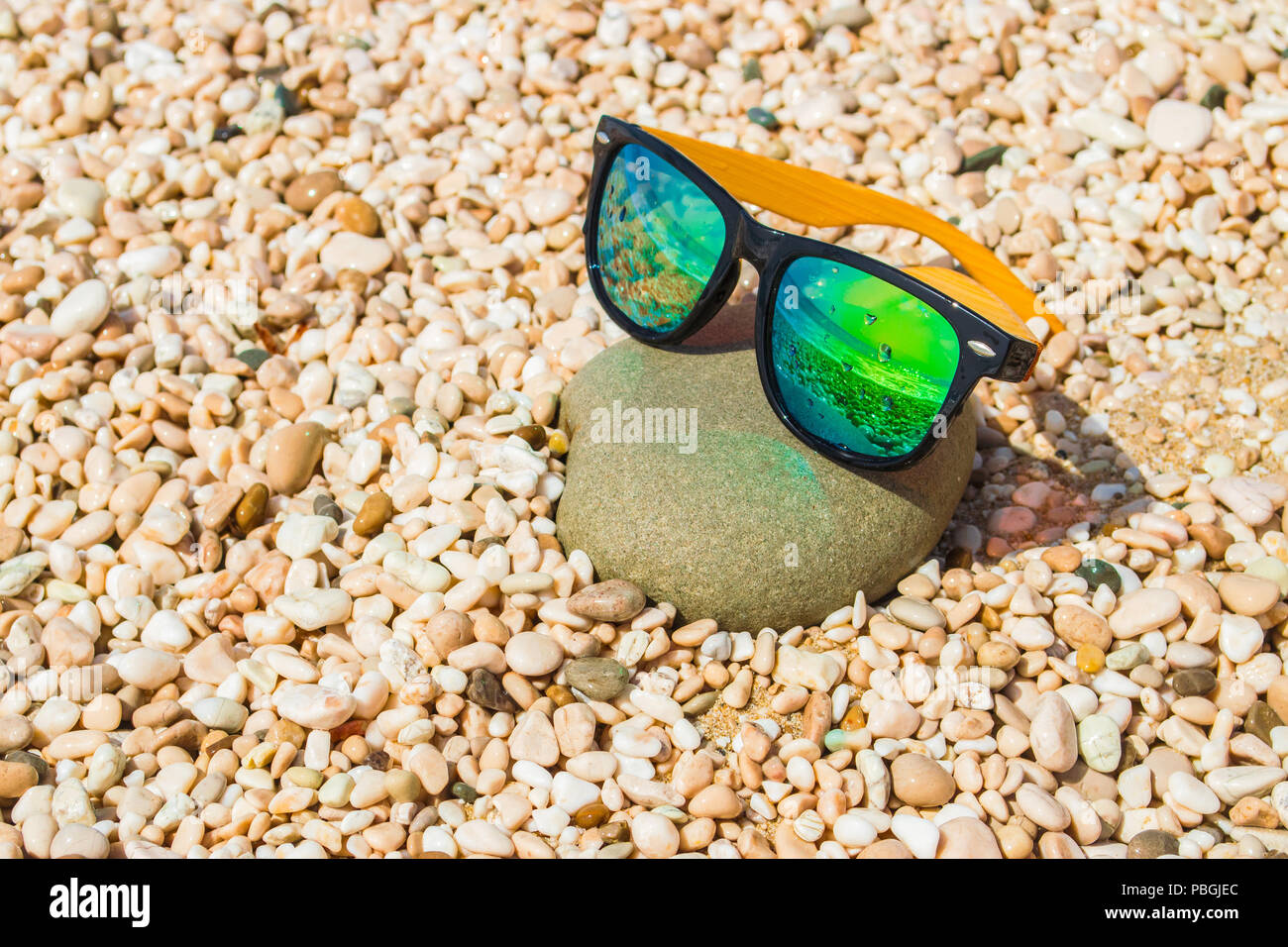 Nass gelbe Sonnenbrille auf einem Kieselstrand spiegelt den Ozean. Sommerurlaub Konzept Stockfoto