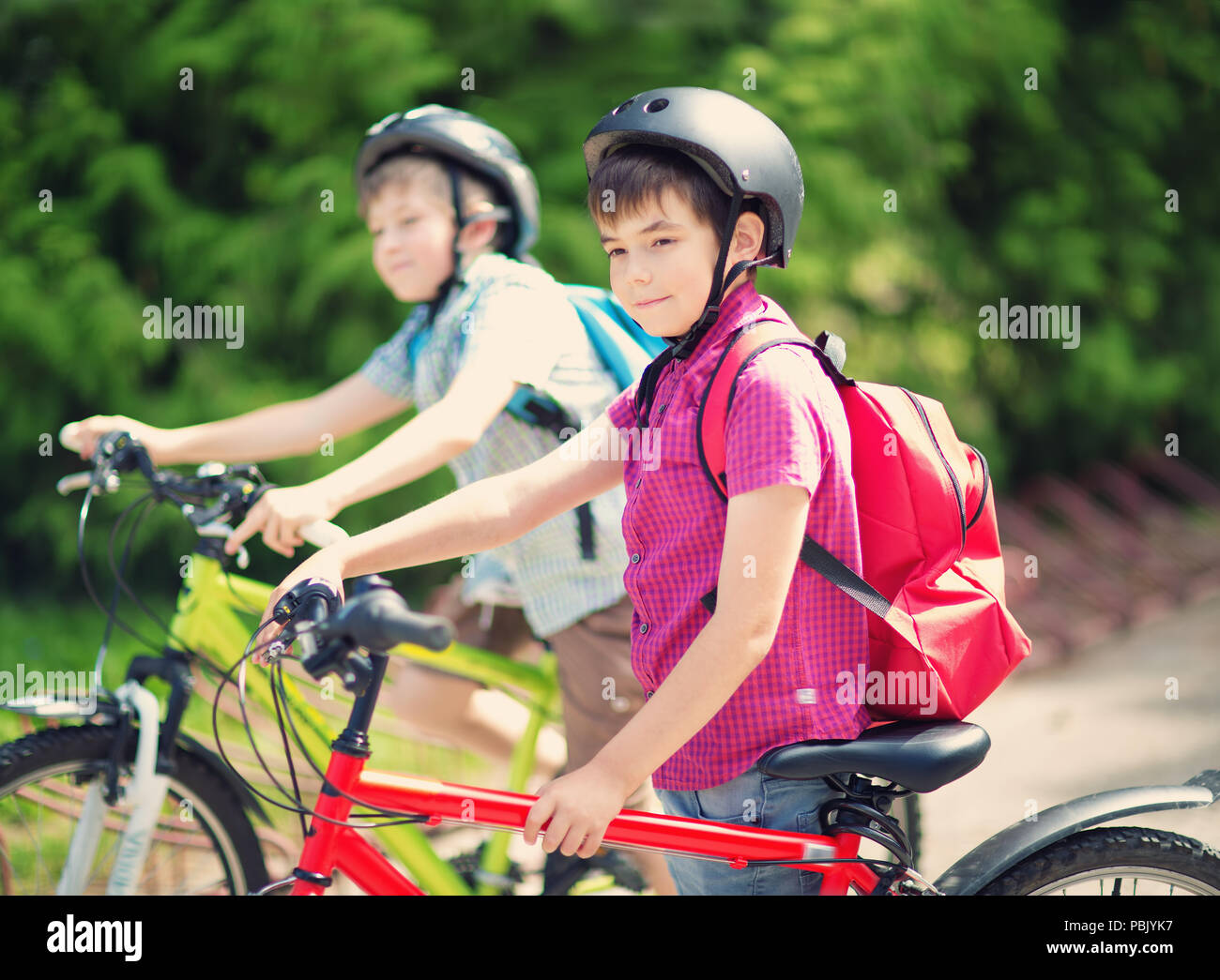 Kinder mit Rucksäcken reiten auf dem Fahrrad im Park in der Nähe der Schule Stockfoto