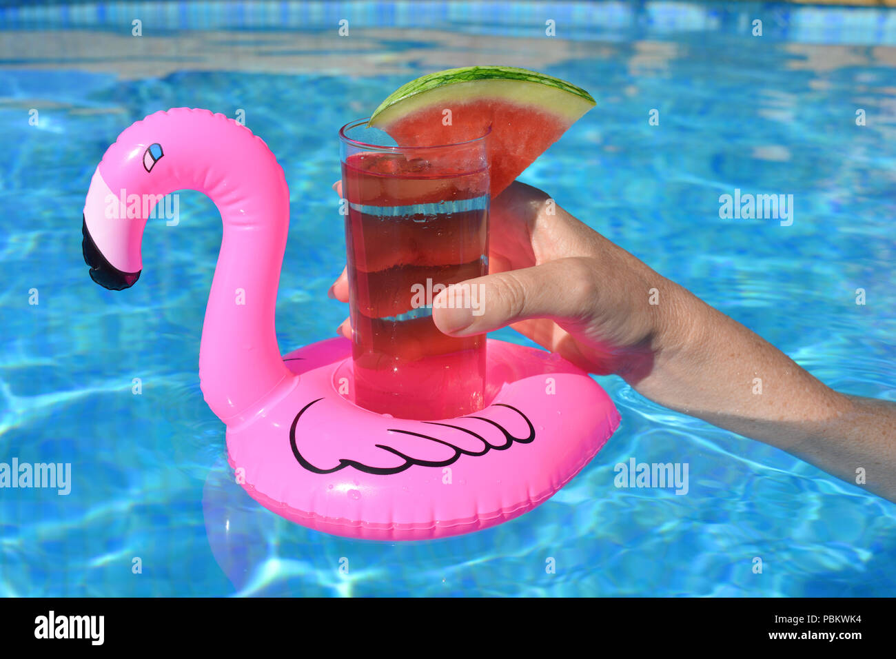 Woman's Hand, mit einem Cocktail in einem aufblasbaren rosa Flamingo schwimmend Getränke Halter in ein Schwimmbad. Sommer Vibes! Stockfoto