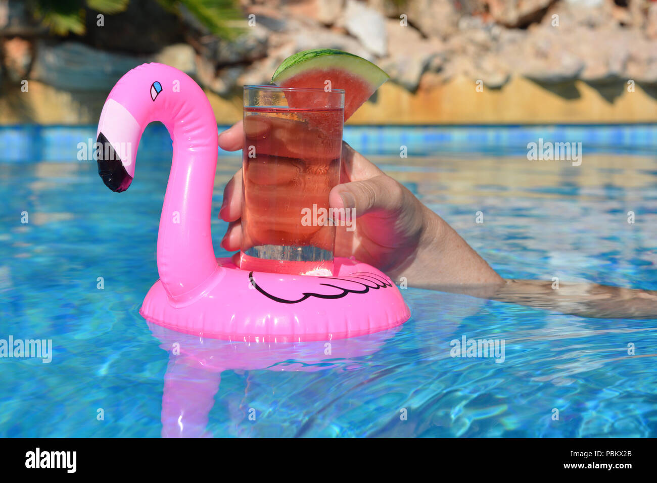 Woman's Hand, mit einem Cocktail in einem aufblasbaren rosa Flamingo schwimmend Getränke Halter in ein Schwimmbad. Sommer Vibes! Stockfoto