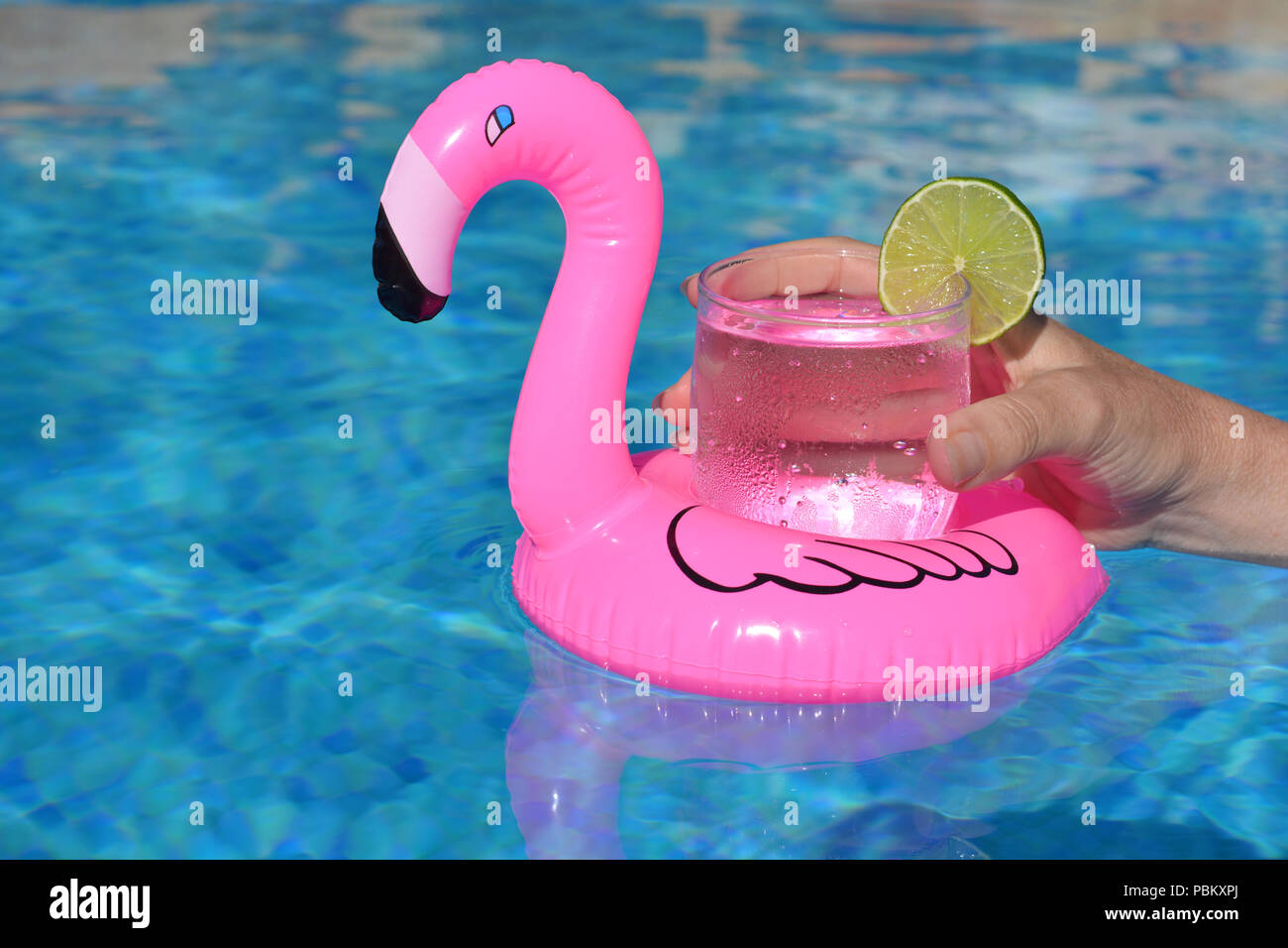 Sommer Vibes! Woman's Hand, mit einem kalten Getränk in einem aufblasbaren rosa Flamingo schwimmend Getränke Halter in einem Pool Stockfoto