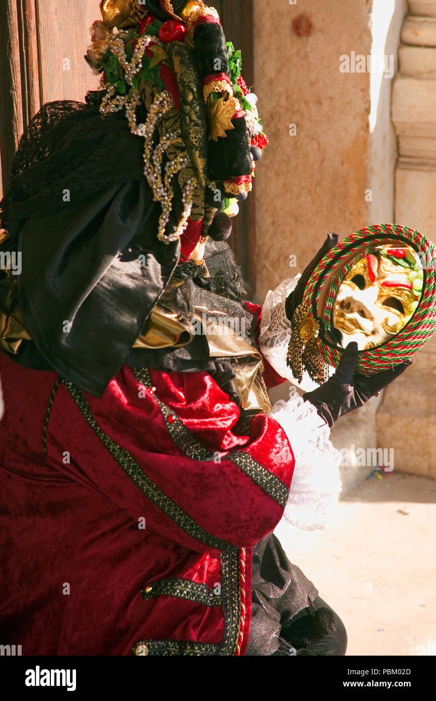 Karneval In Venedig: Piazzetta San Marco, Venedig, Italien. Maskierte Nachtschwärmer posiert mit einem Spiegel unter den Arkaden des Palazzo Ducale Stockfoto