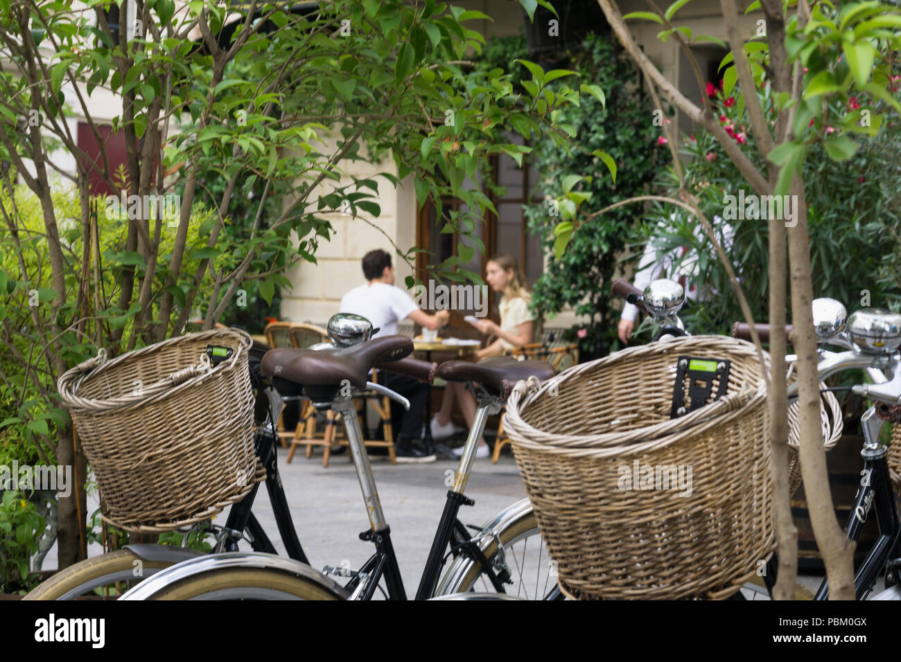 Paris Paar - Ein Paar aus der Distanz mit Frühstück gesehen auf einem typischen Pariser Straße. Zwei Fahrräder mit weidenkörbe sind in der Nähe geparkt. Stockfoto