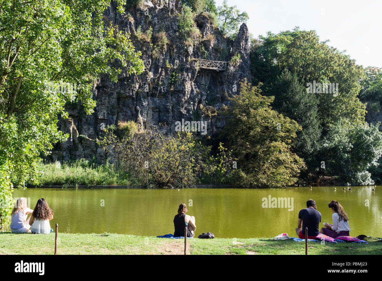 Paris Park mit See - Menschen entspannend in der Nähe der See im Park des Buttes Chaumont in Paris, Frankreich, Europa. Stockfoto