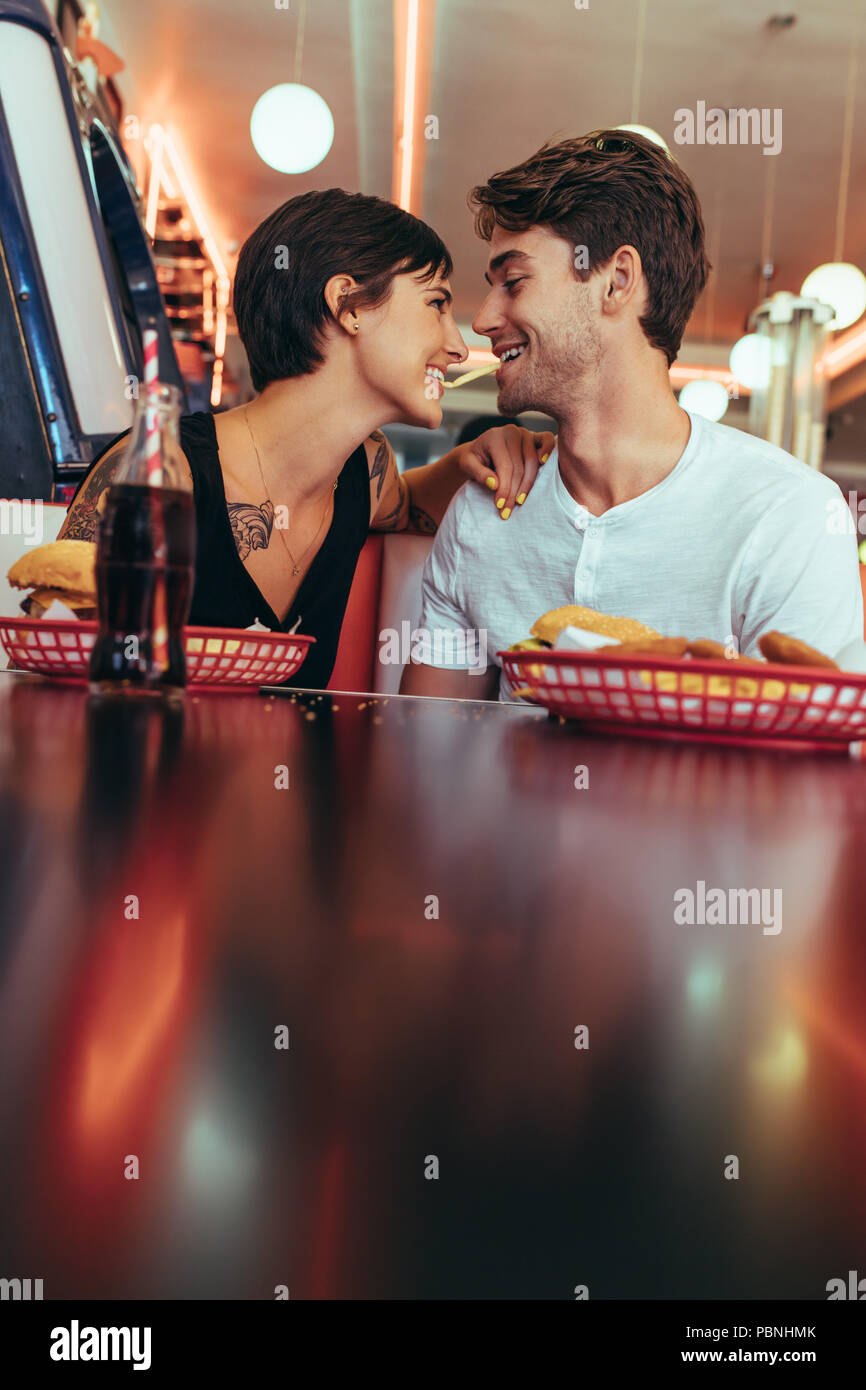 Romantisches Paar speisen in einem Restaurant mit Speisen und alkoholfreie Getränke auf dem Tisch. Lächelnd Mann und Frau teilen ein Pommes Frites es in Ihren zwischen Holding Stockfoto