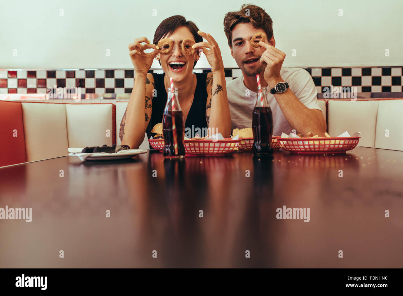 Romantisches Paar in einem Restaurant sitzen und Spaß holding Keks Ringe um die Augen. Lächelnd Mann und Frau zu einem Diner mit Nahrungsmitteln und sof Sitzen Stockfoto
