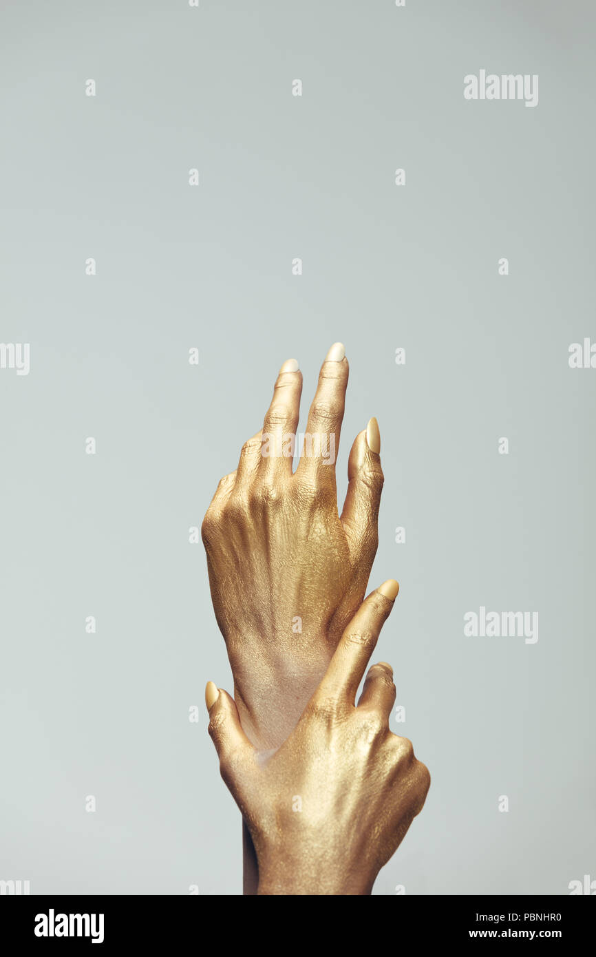 Weibliche Hände in Gold Farbe auf grauem Hintergrund. Hände von Frau mit goldener Farbe bemalt. Stockfoto