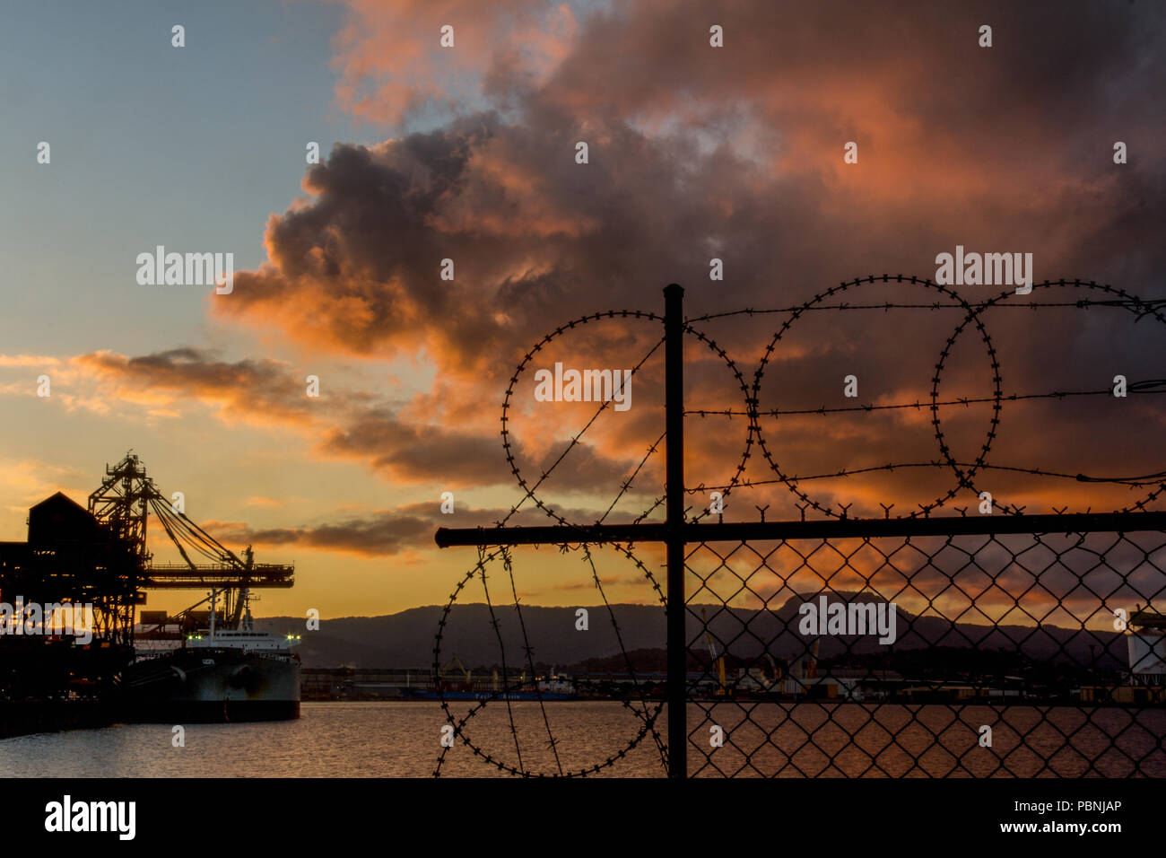 Querformat der industriellen Hafen schießen durch Silhouette von Stacheldraht / barbed wire Barriere mit Annäherung an den Abend Sturm Stockfoto