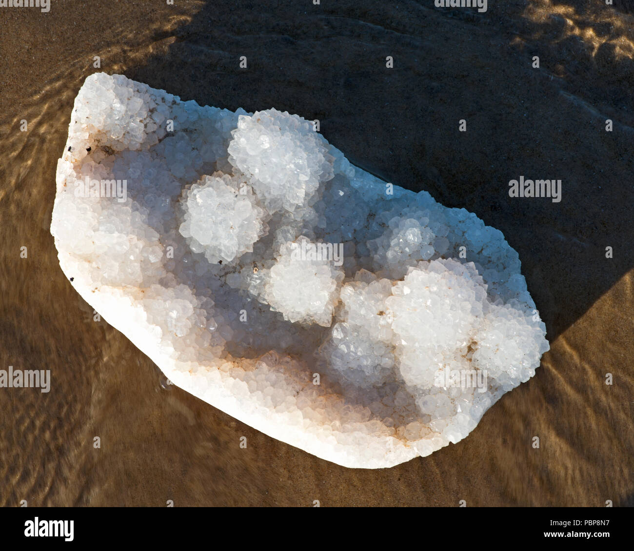 Aurora Rainbow Quartz Cluster aus Indien liegen auf nassem Sand vor dem See bei Sonnenaufgang. Stockfoto