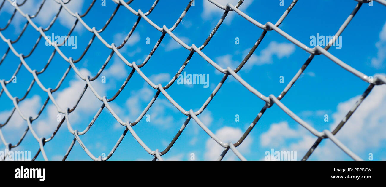 Ein Zaun aus Drahtgeflecht, Verrechnung mit Weiß auf dem Hintergrund der blauen Himmel und Sonnenschein Stockfoto