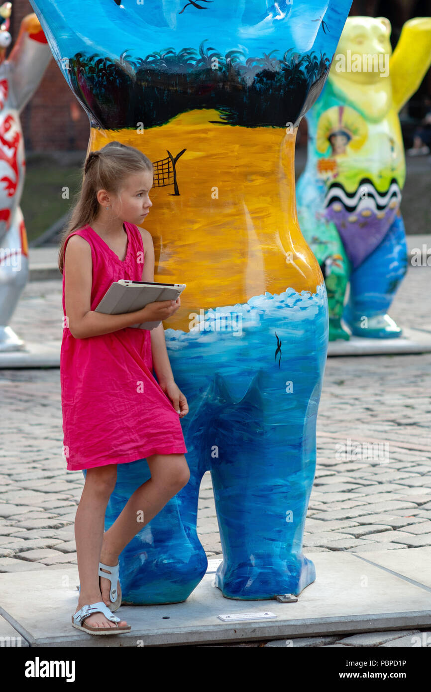 RIGA, Lettland - 26. JULI 2018: United Buddy Bears Ausstellung. Ein Mädchen mit einem Tablett in den Händen steht an der Bär Skulptur. Stockfoto