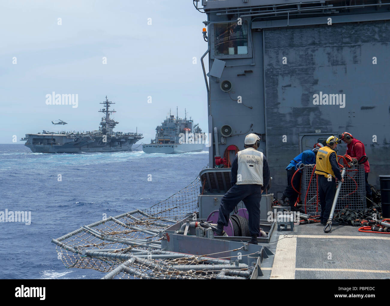 180720-N-JAHRE 245-0492 PAZIFISCHER OZEAN (20 Juli 2018) Segler aus der Geführten-missile Cruiser USS Lake Champlain (CG57), für Lieferungen auf dem Flugdeck Vorbereiten während einer vertikalen Auffüllen aus dem Aux Dry Cargo und Munition ship USNS Charles Drew (T-AKE 10) Während der Pacific Rim (Rimpac) Übung, Juli 20. In der Ferne, Drew Pumpen Kraftstoff zu den Flugzeugträger USS Carl Vinson (CVN 70) und sendet liefert per Hubschrauber. 25 Nationen, mehr als 45 Schiffe und u-Boote, und etwa 200 Flugzeugen und 25.000 Mitarbeiter sind teilnehmenden RIMPAC vom 27. Juni bis 2. August in und Aro Stockfoto