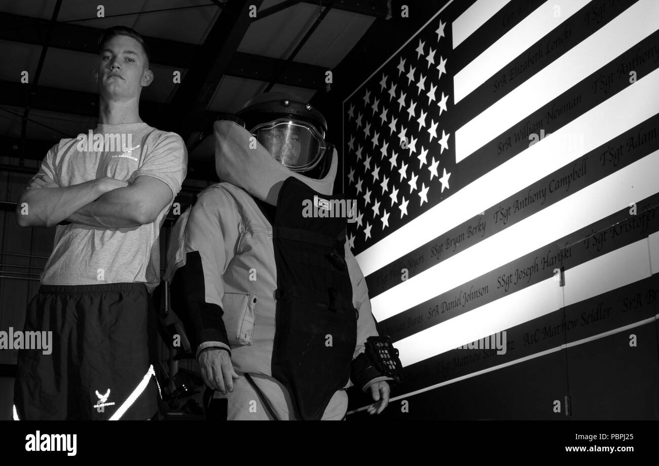 Us Air Force Staff Sgt. Jordan Massey, 20. Bauingenieur Squadron (CES) Beseitigung von Explosivstoffen (EOD) Handwerker, steht in einer Bombe Anzug neben Airman 1st Class Evan Kühlung, 20. CES EOD Lehrling, bevor ein Flag Wandbild mit den Namen der Gefallenen EOD Techniker in Ihrer Turnhalle bei Shaw Air Force Base, S.C., 23. Juli 2018. Die Mauer erinnert die 20. CES Flieger der Opfer andere EOD Mitglieder gemacht haben und warum Sie müssen sich besser arbeiten. (U.S. Air Force Foto von älteren Flieger Kathryn R.C. Reaves) Stockfoto