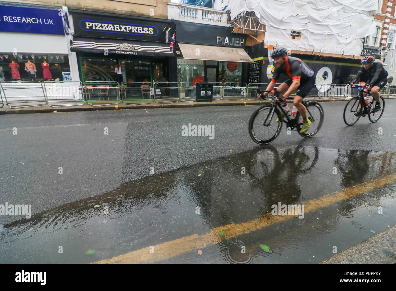 London, Großbritannien. 29. Juli 2018. Radfahrer durch Wimbledon Village in der aufsichtsrechtlichen London Surrey 100 Classic Event in nassen Bedingungen wie die Regenzeit, unten zu kommen. Die aufsichtsrechtlichen Fahrt London-Surrey 100 in seiner sechsten Jahr feiert das Vermächtnis für die London 2012 die Olympischen und Paralympischen Spiele erstellt Radfahren und folgt einer 100km Route auf geschlossenen Straßen durch das Kapital und in die Landschaft von Surrey Credit: Amer ghazzal/Alamy leben Nachrichten Stockfoto