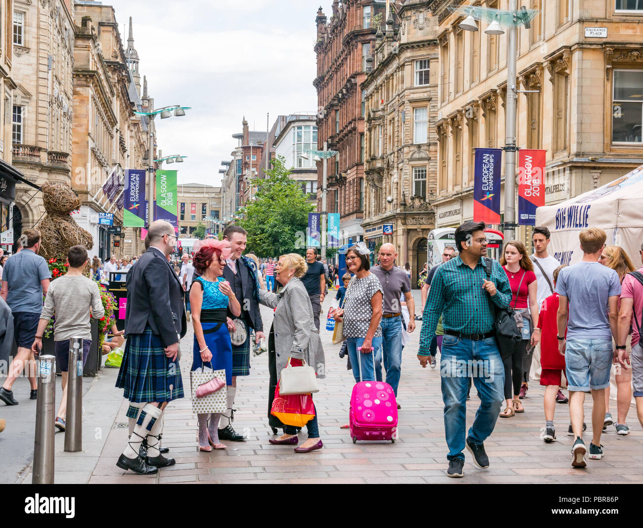 Die Menschen gekleidet für eine Hochzeit mit Männer in Kilts anhalten, um Hallo zu sagen und Begrüßung in einer belebten Straße, Buchanan Street, Glasgow, Schottland, Großbritannien Stockfoto