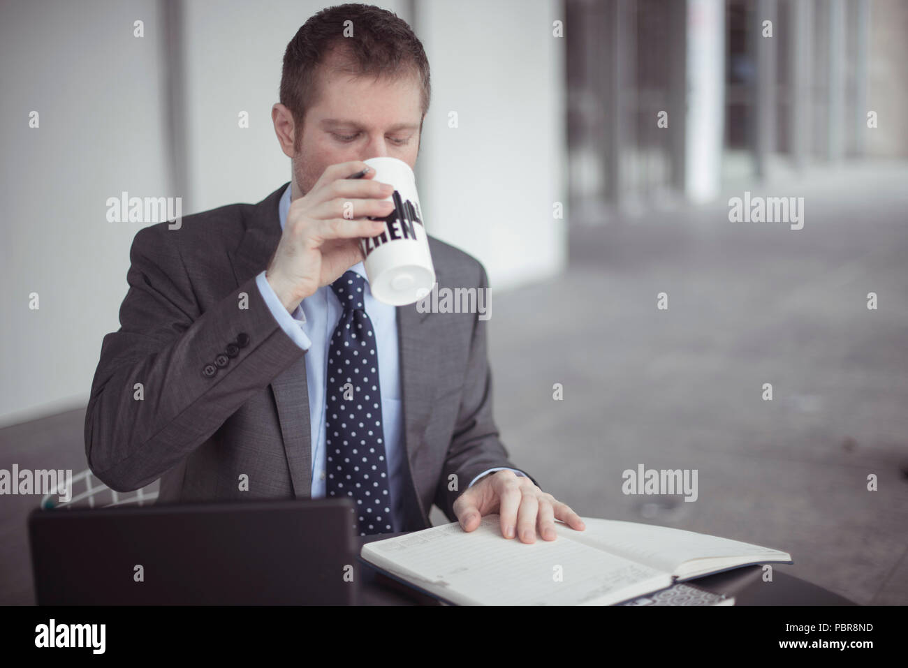 Von Mitte 30 kaukasischen Mann in Anzug und Krawatte, trinken Kaffee, der mit seinem Computer und ein Notebook in ein Cafe. Stockfoto