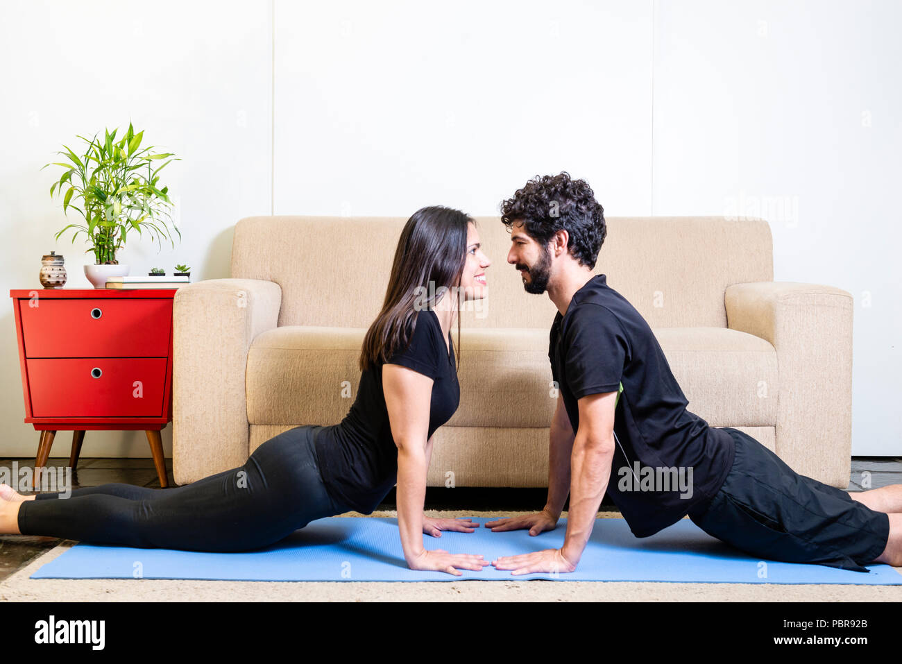 Schöne hetero kaukasischen Paar in schwarzer Kleidung auf Blau yogamat nach oben tun - schauenden Hund darstellen Stockfoto