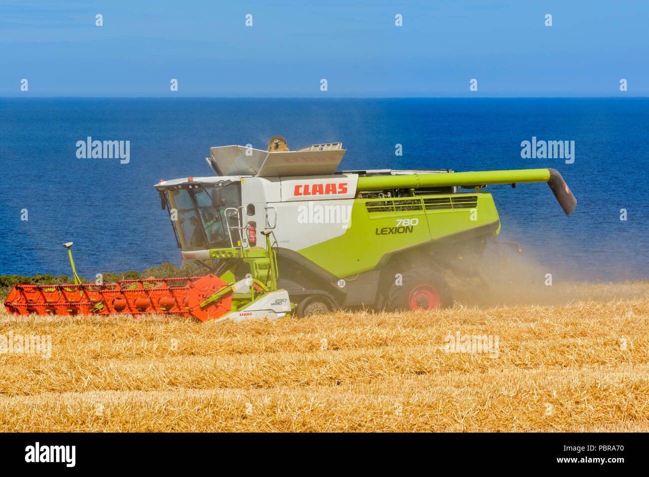 Mähdrescher auf einem GERSTENFELD MIT BLICK AUF DAS MEER UND den Moray Firth SCHOTTLAND Stockfoto