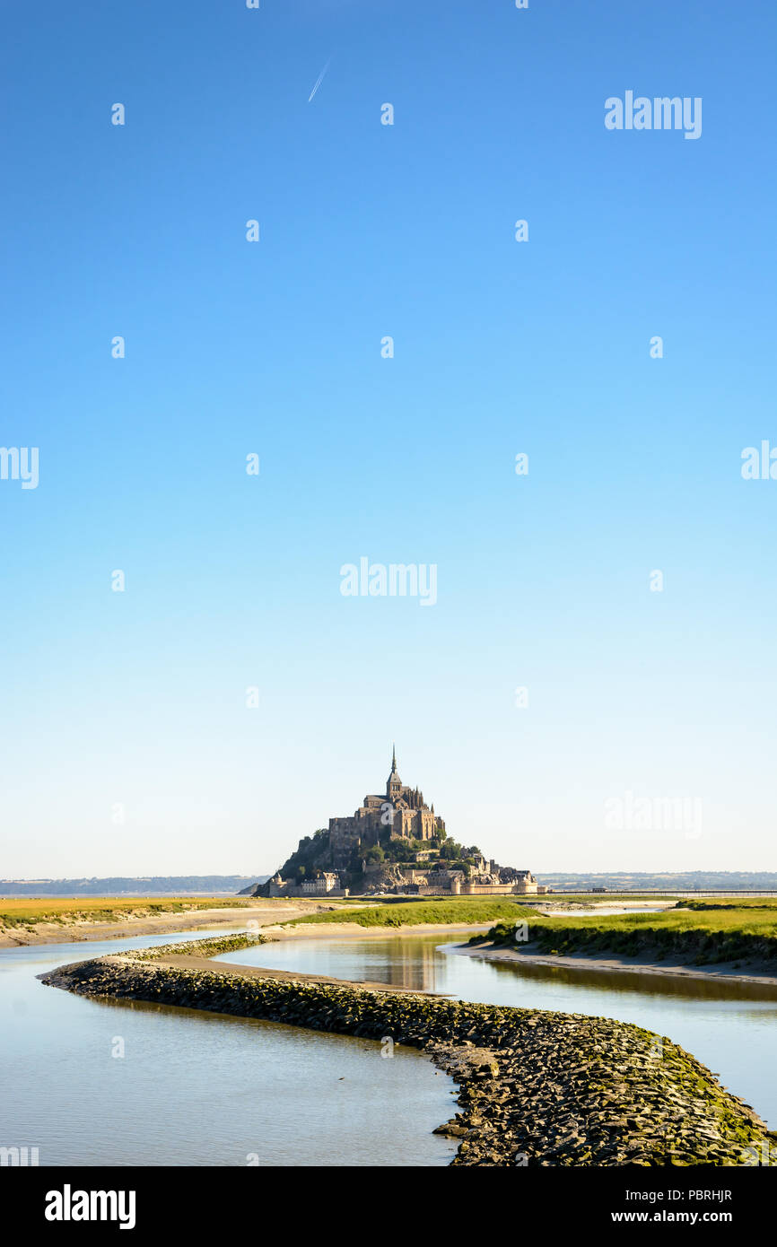 Der Mont Saint-Michel tidal Island, in Frankreich in der Normandie gelegen, mit einem Stein Damm auf der Couesnon river im Vordergrund unter einem tiefblauen Himmel. Stockfoto