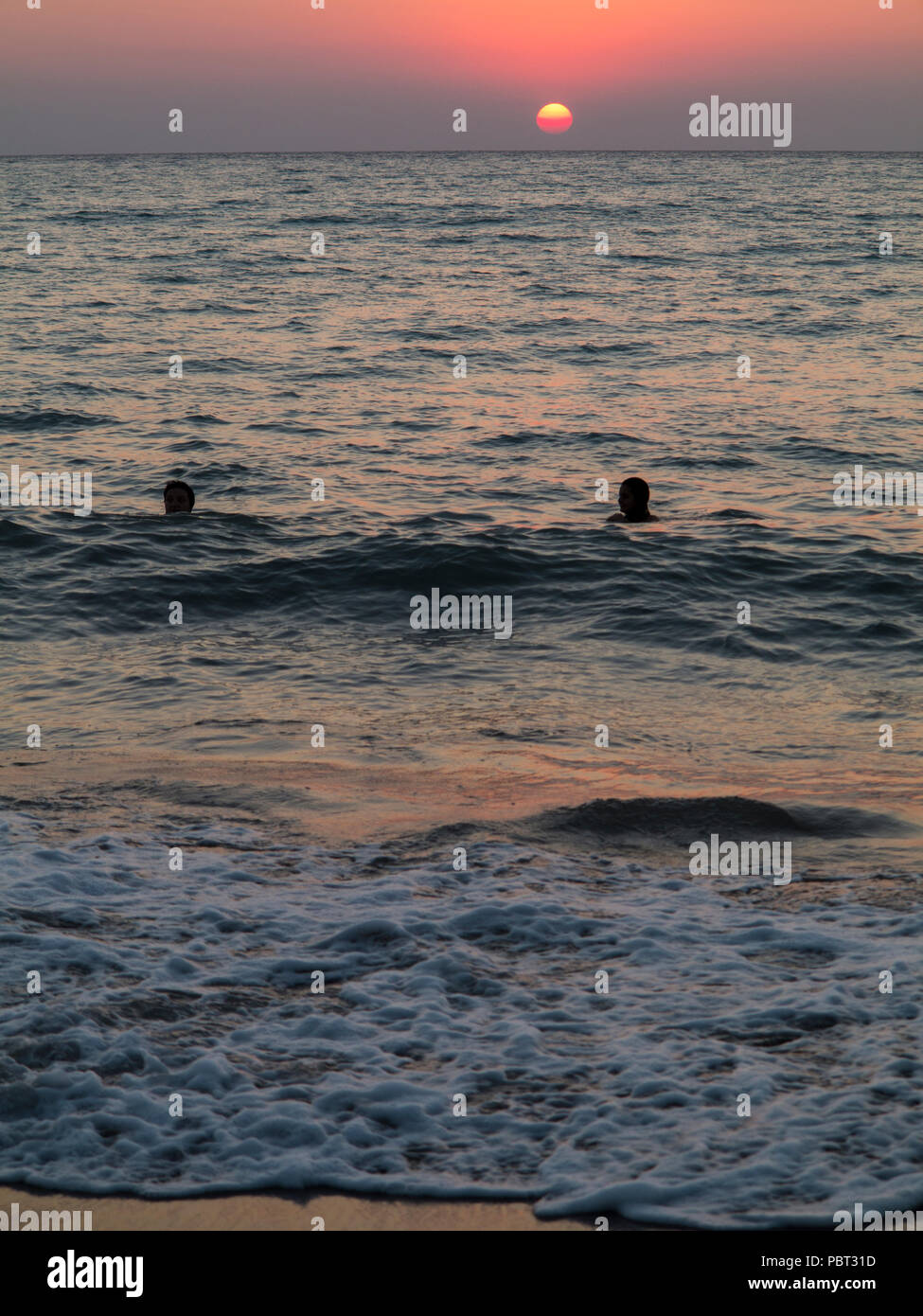 Zwei Personen genießen Sie den letzten Tag am Abend mit einem Schwimmen wie die Sonne am Horizont setzt Stockfoto