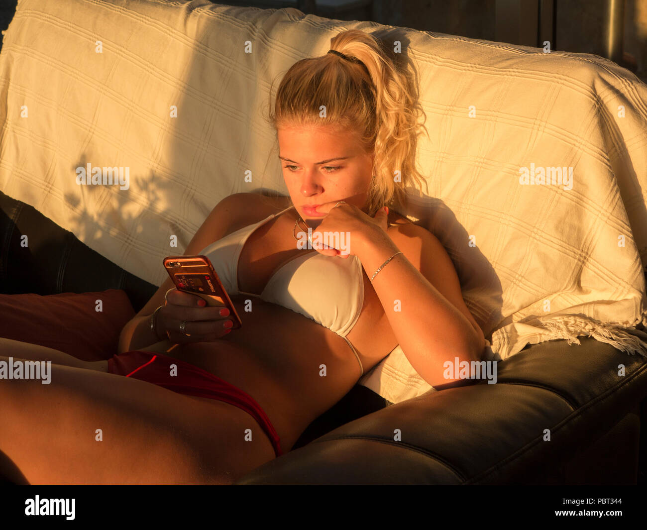 Eine hübsche blonde Mädchen ihr Telefon Kontrolle in einem Bikini in einem Haus Stockfoto