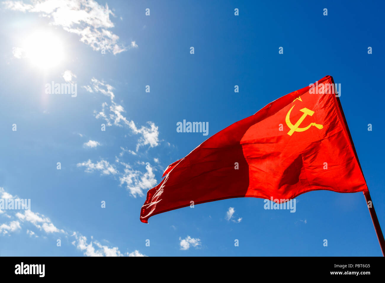 Red kommunistische Flagge der UDSSR gegen den blauen Himmel mit weißen Wolken und Sonne. Stockfoto