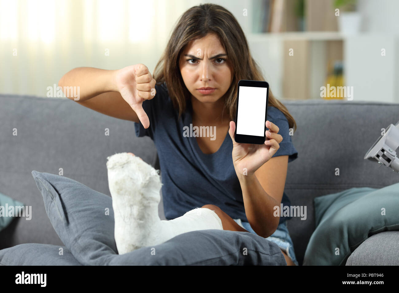 Verärgert behinderte Mädchen zeigt einen leeren Bildschirm "Telefon" auf einer Couch im Wohnzimmer zu Hause sitzen Stockfoto