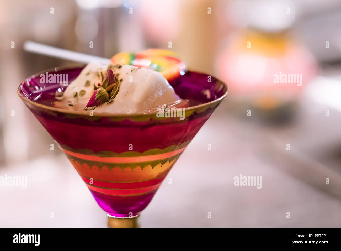Alkoholfreien Cocktail in rot gemusterten Glas mit Ice Cube, chemische rose Blumen und Süßigkeiten auf der Theke. Süße Lust auf wenig Alkohol trinken. Stockfoto