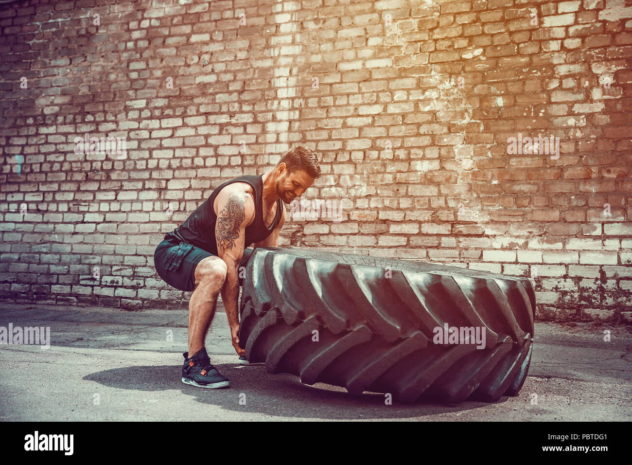 Muskulöse bärtigen tätowiert fitness Mann, die große Reifen in street Gym. Konzept heben, Workout Ausbildung. Stockfoto