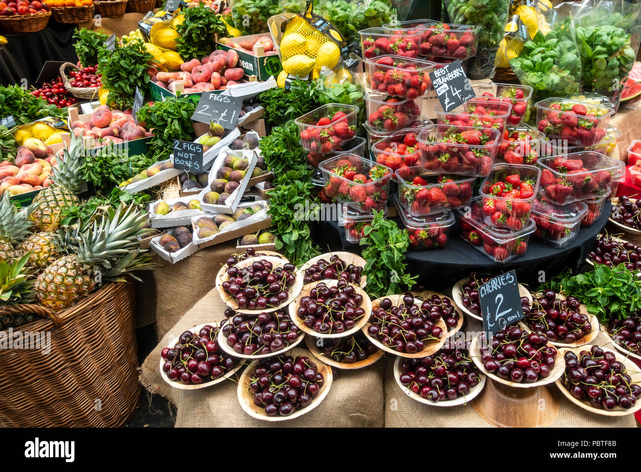 Eine Auswahl an Obst, Feigen, Kirschen, Erdbeeren, Pfirsiche, Nektarinen, Zitronen und Kräutern auf Verkauf im berühmten und historischen Borough Market, London. Stockfoto