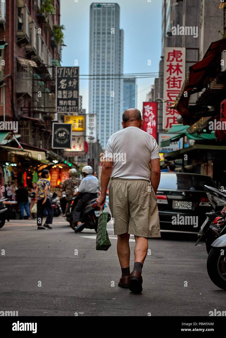 Ein alter armer Mann zu Fuß auf den asiatischen Markt mit Wolkenkratzern auf dem Hintergrund Stockfoto