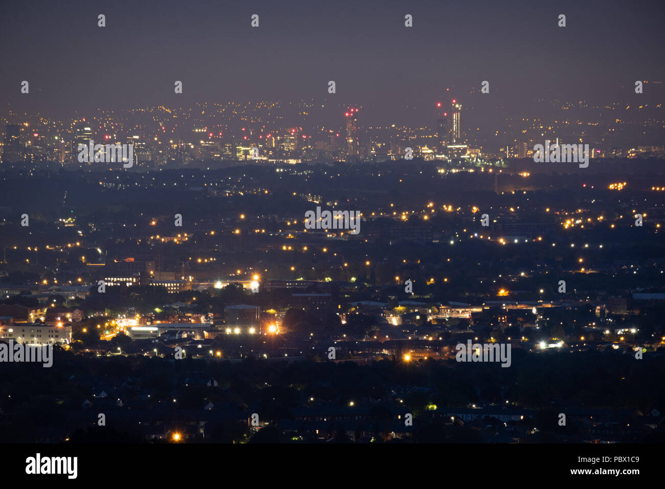 Nacht Blick von der Stadt Manchester, UK unten und aus der Ferne mit einem weiten Blick über die Lichter von Winter Hill, Bolton genommen Stockfoto
