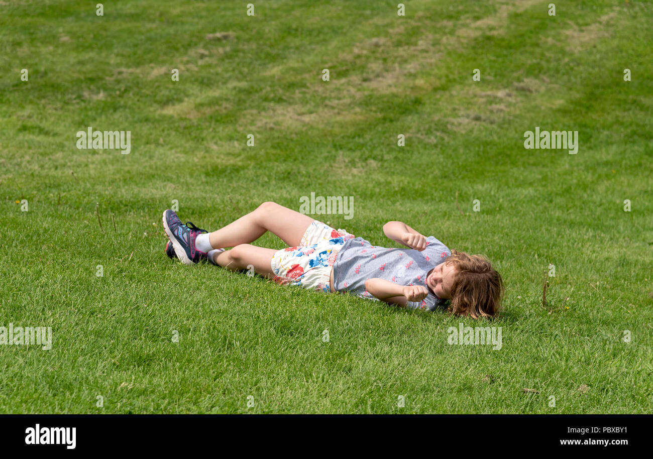 Kinder spielen in Rollen hinunter einen grasbewachsenen Hügel Stockfoto