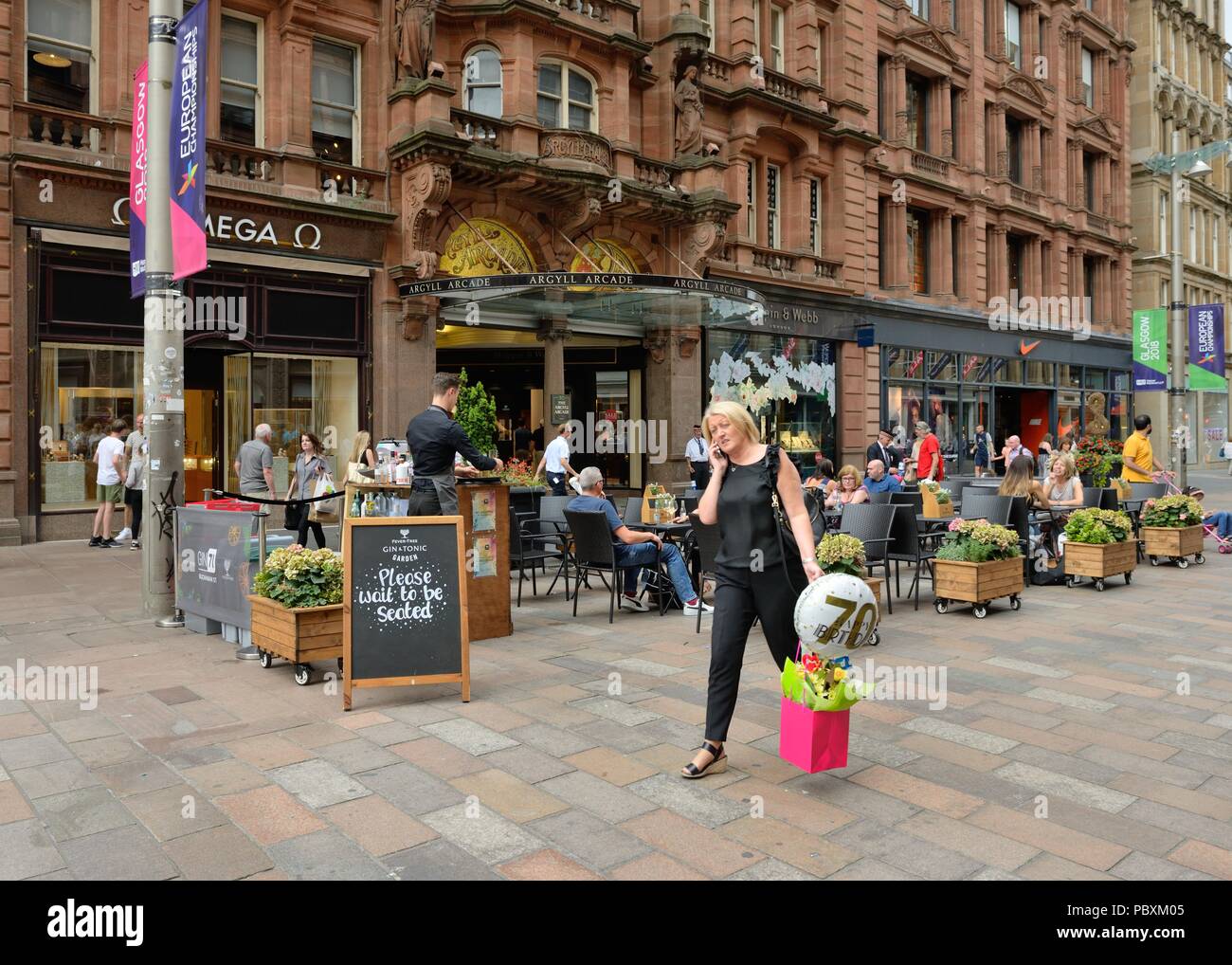 Eine Frau auf dem Handy shopping Geburtstagsgeschenke außerhalb Argyll Kammern auf der Buchanan St. Fußgängerzone, das Stadtzentrum von Glasgow, Schottland, Großbritannien Stockfoto
