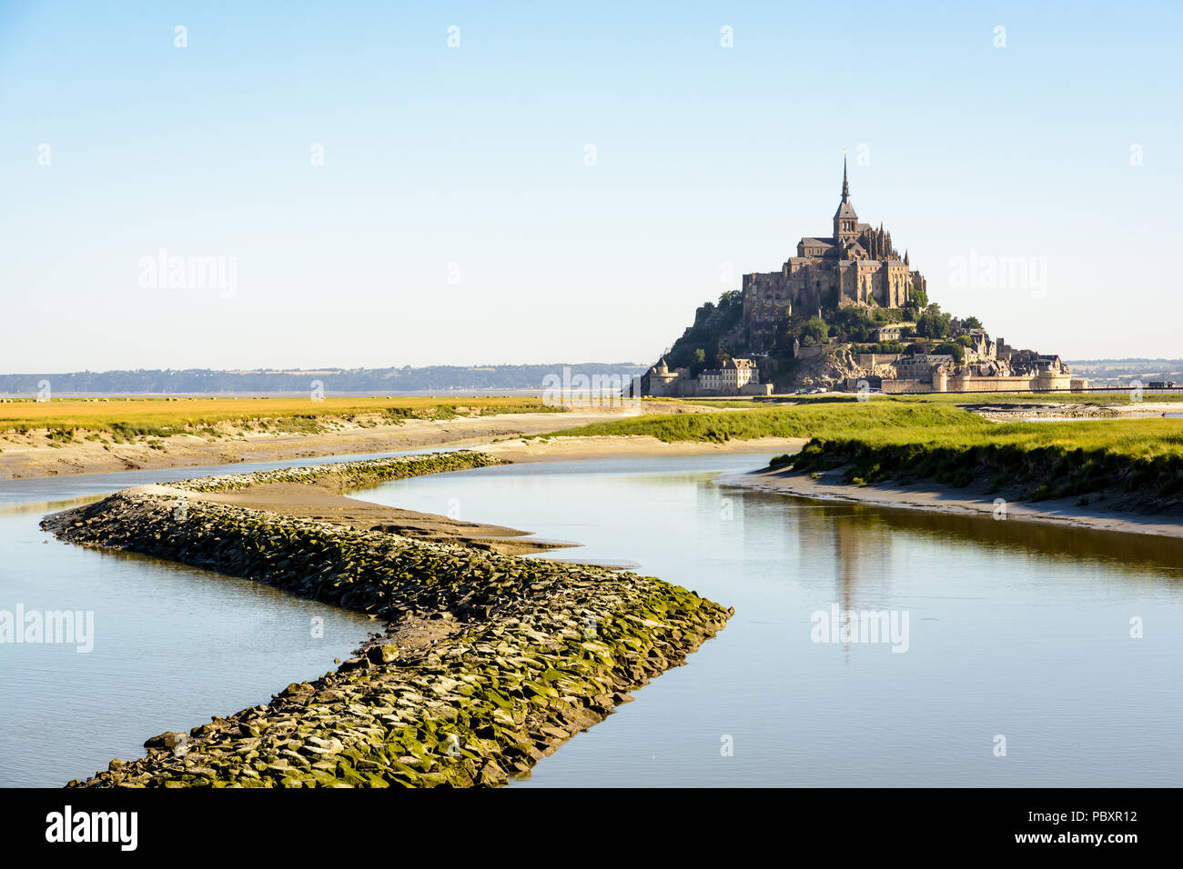 Der Mont Saint-Michel tidal Island, in Frankreich in der Normandie, bei Flut mit einem Stein Damm auf der Couesnon river im Vordergrund. Stockfoto