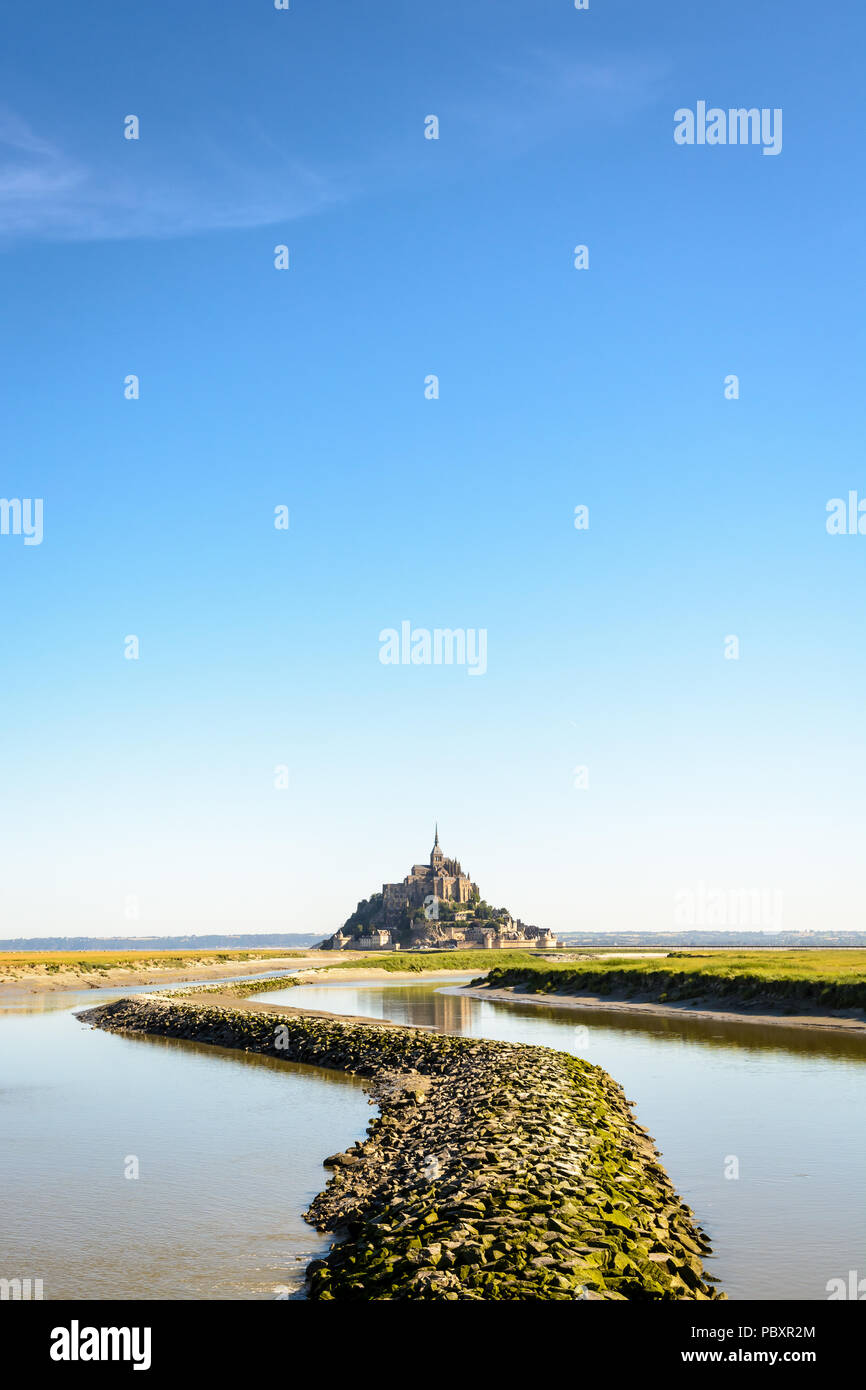 Der Mont Saint-Michel tidal Island, in Frankreich in der Normandie gelegen, mit einem Stein Damm auf der Couesnon river im Vordergrund unter einem tiefblauen Himmel. Stockfoto