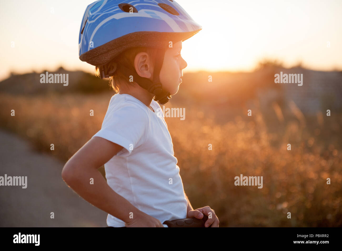 Cute gesundes Kind im Sport Helm mit Scooter auf leere Straße am Sunset Stockfoto