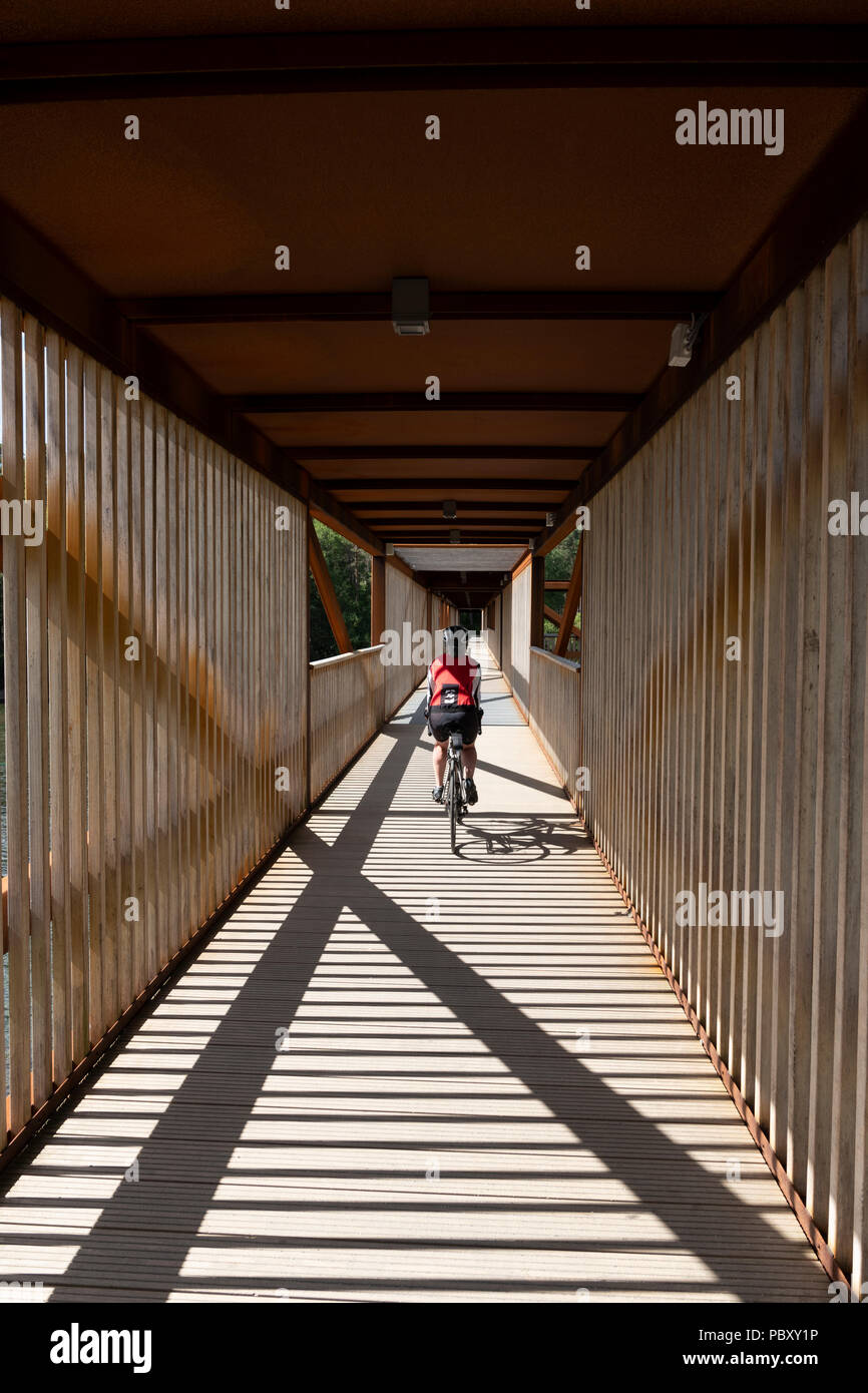 Eine weibliche Radfahrer Kreuzung eine überdachte Holzbrücke in Norwegen Stockfoto
