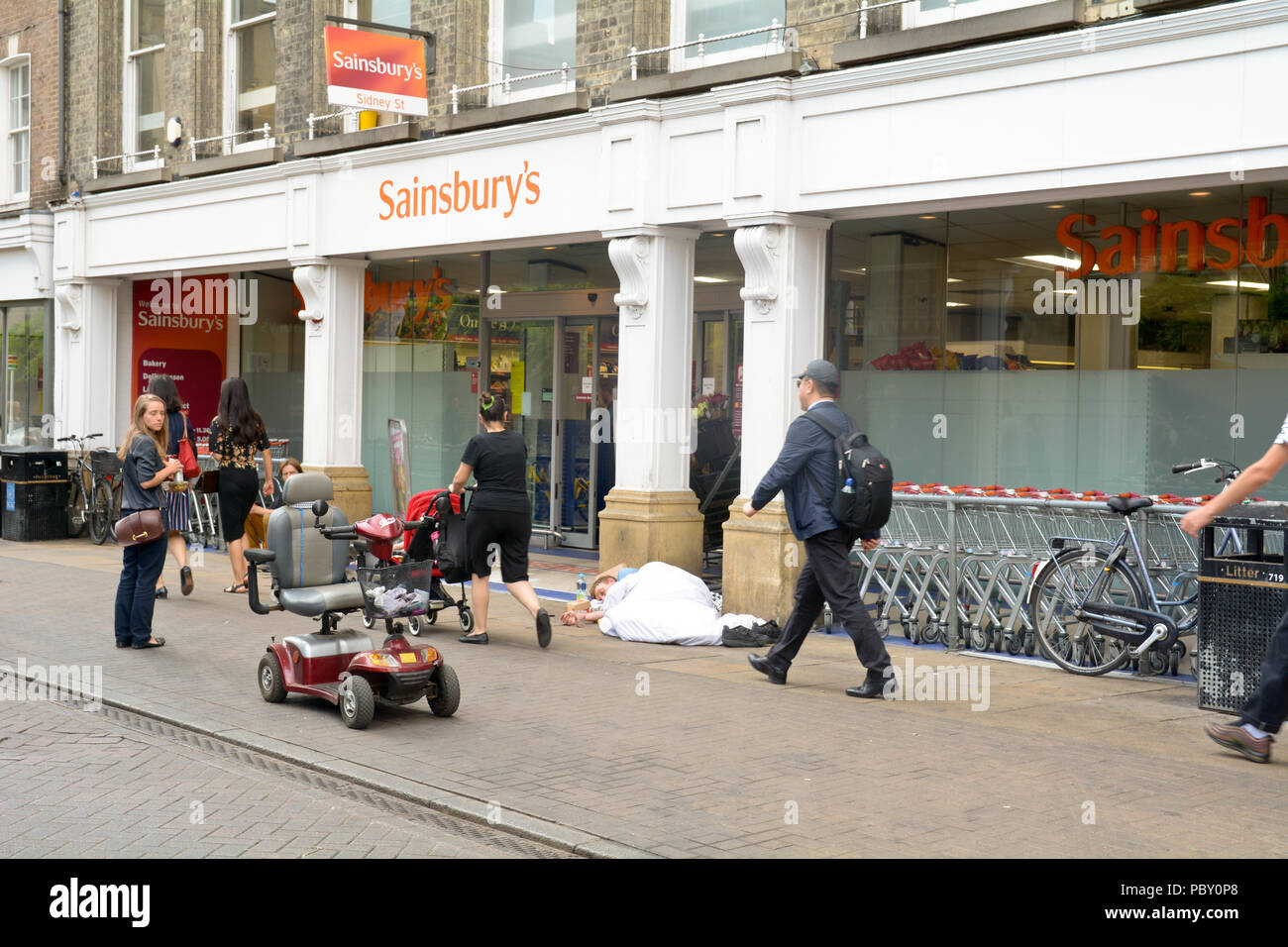 Obdachlosen schläft und ein weiteres Betteln außerhalb Sainsbury's Supermarkt in der Innenstadt von Cambridge, Cambridgeshire, England Stockfoto