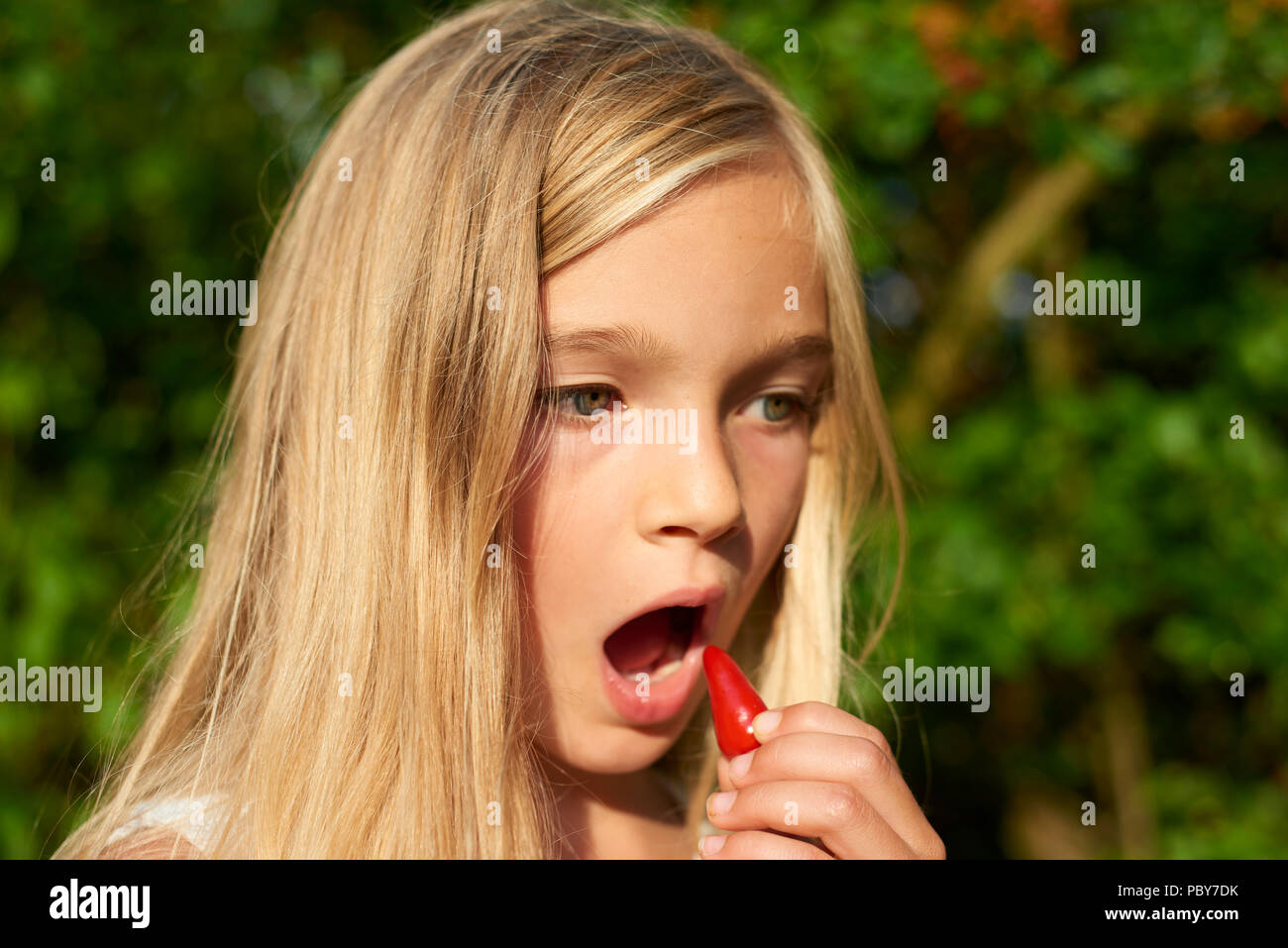 Kind cute girl Holding frisches rohes Chili und Vorbereitung es draußen im Sommer Garten zu essen. Grüner Hintergrund Stockfoto