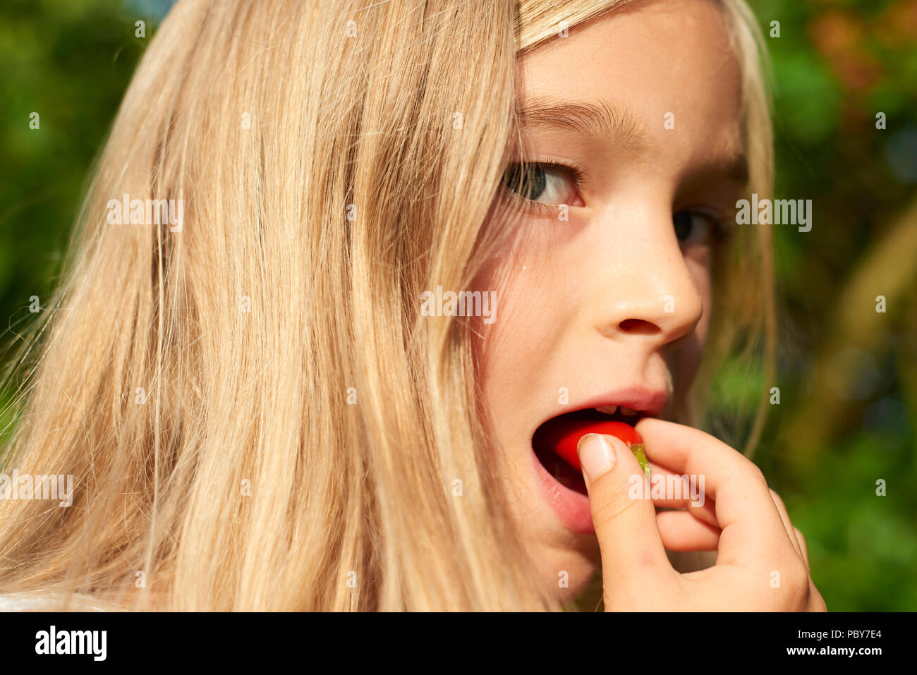 Kind cute girl Holding frisches rohes Chili und Vorbereitung es draußen im Sommer Garten zu essen. Grüner Hintergrund Stockfoto